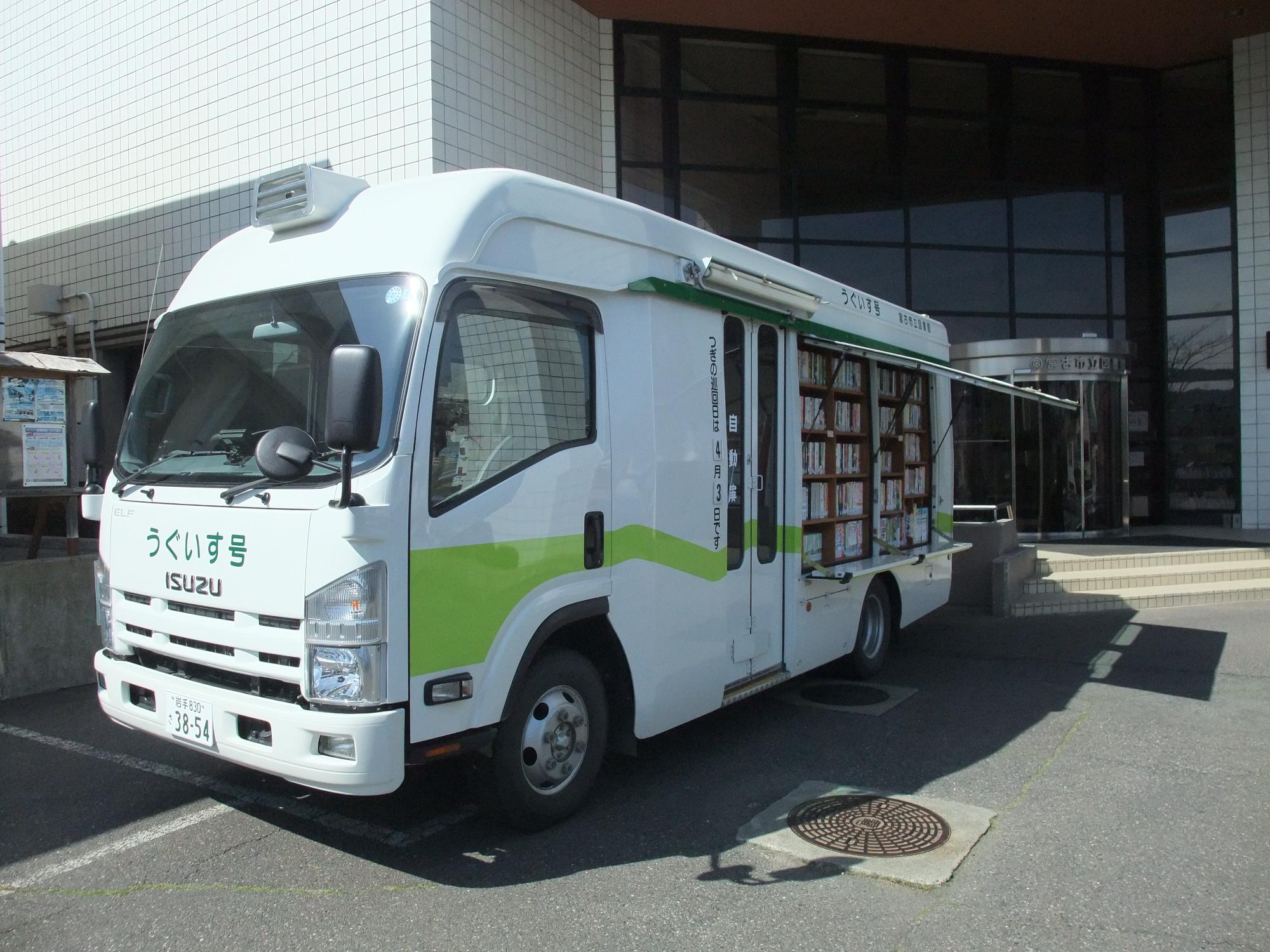 白色に黄緑色のアクセントが塗装されている車体が特徴でフロント箇所に「うぐいす号」とかかれているバスが本が陳列されているところが見えるように車体の後方部分が上開きに開いている様子を撮影した写真