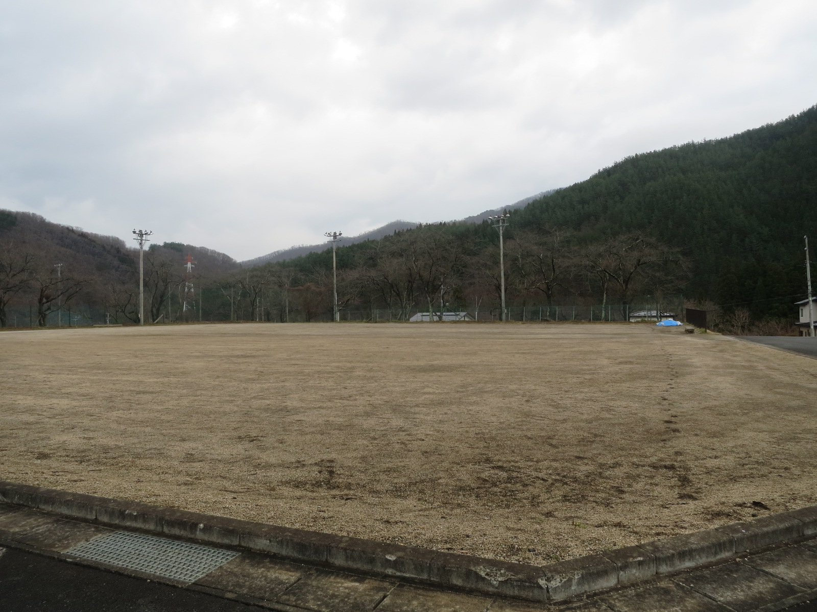 周りを山々に囲まれ後方には照明塔が3台設置されたグラウンドの写真