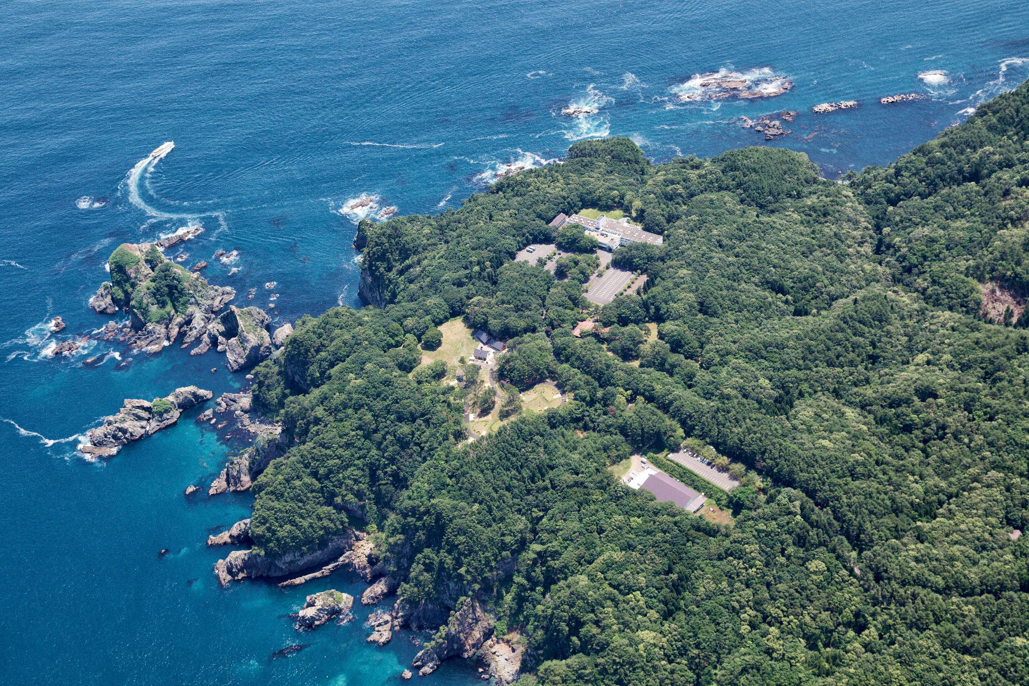 海が臨め、周りを岩壁と木々に囲まれた休暇村陸中宮古を上空から撮影した写真
