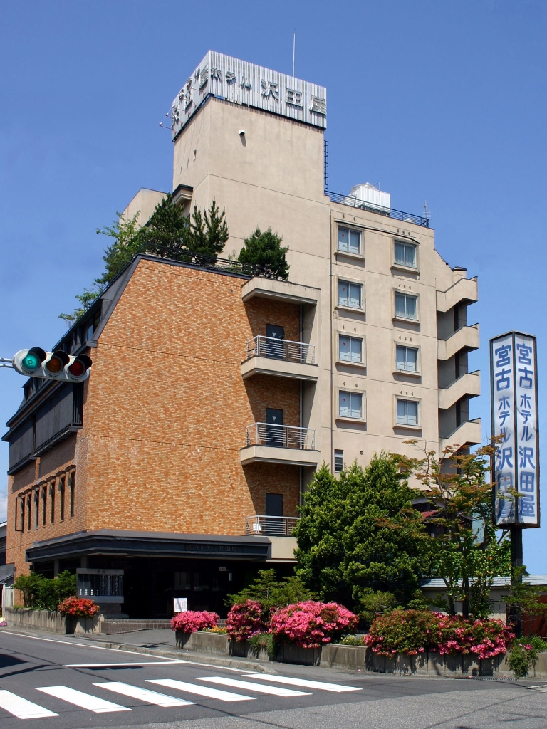 屋上と建物前に「宮古ホテル沢田屋」と書かれた看板が設置され出入口やバルコニーに植物がたくさん植えられている外壁が茶色とクリーム色の宮古ホテル沢田屋の外観写真