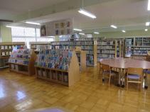 読書ができる丸テーブルと椅子が数脚置かれ、大小ある背丈の本棚が設置され沢山の本が陳列されている図書室内の写真