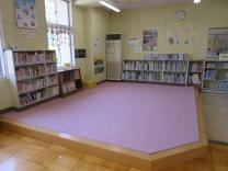ピンク色のカーペットが敷かれた小上がりの広間に背丈が低い本棚が数台設置されているカーペットコーナーの写真