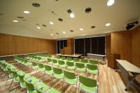 1列に10脚ほどの緑色の椅子が4列並び、壁に沿って長テーブルが置かれている多目的ホール内の写真