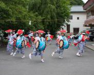 花の飾りを頭にかぶり太鼓を担いだ着物を着た演者たちが踊っている写真
