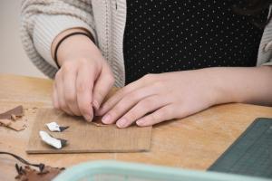 女性が四角い板の上で革を切ってキーホルダー作りをしている手元をアップで撮影した写真
