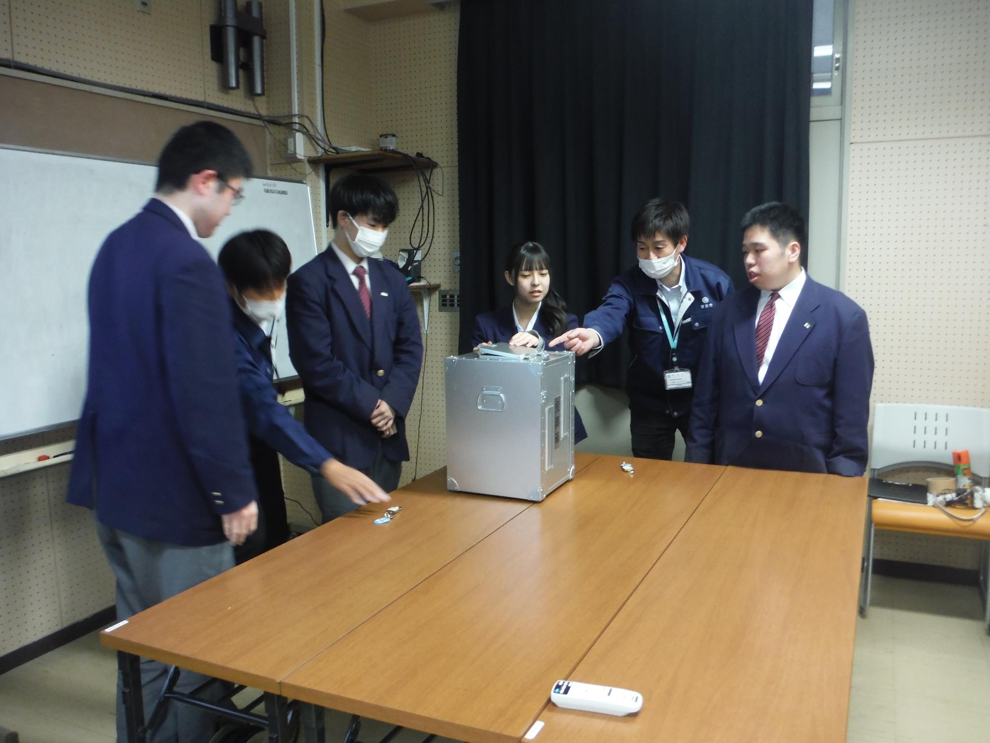 長机の上で投票された用紙を開票作業している3名の男性の写真