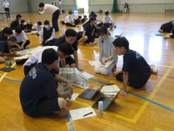 5名で円になり座り新聞のようなものを見ながら話をしている写真