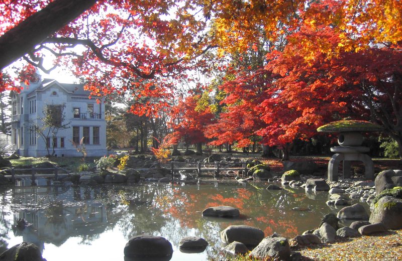 奥には白い2階建ての洋館があり、手前の池にはとても大きな雪見灯籠や赤や黄色の色鮮やかな紅葉が美しい写真