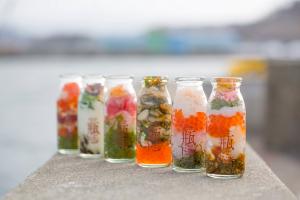 主に海鮮系のものが多い、宮古市の旬の食材を瓶ドンという文字が入った牛乳瓶に入れた商品が、野外で並べられている写真