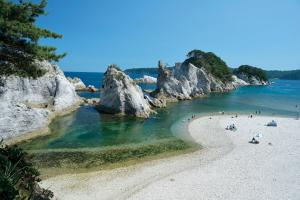 快晴の下、水面上に巨大な岩礁が並んでいる浄土ヶ浜で、複数の人が海水浴をしている様子が小さく映っている写真