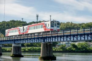 白い車体に赤色の波打ったラインが入った2両の電車が鉄道橋を走行している写真