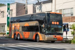 茶色の車体にオレンジ色の水玉模様と、その中にMEXと白色で書かれた二階建てバスが道路を走行している写真