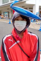 白いマスクをして赤い薄手の運動着を着ている女性を正面から写した写真