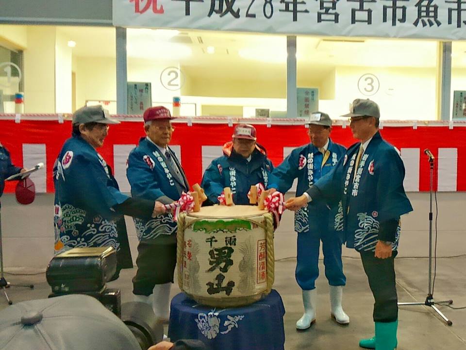 帽子を被り法被を着た市長と4名の男性が、日本酒の大きな樽を鏡開きしている様子の写真