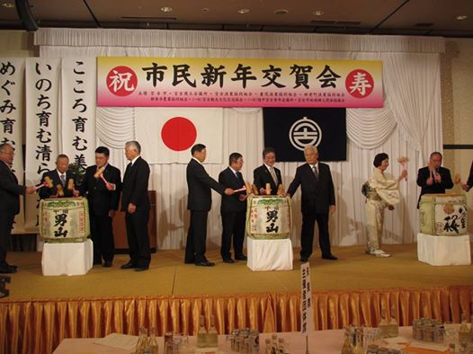 舞台の上で3つの大きな日本酒の樽を鏡開きしている様子の市長と関係者の方々の写真
