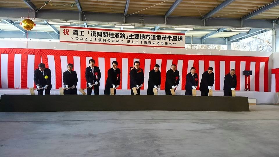 紅白幕の前に関係者の男性が10名並び、全員で鍬入れをしている様子の写真