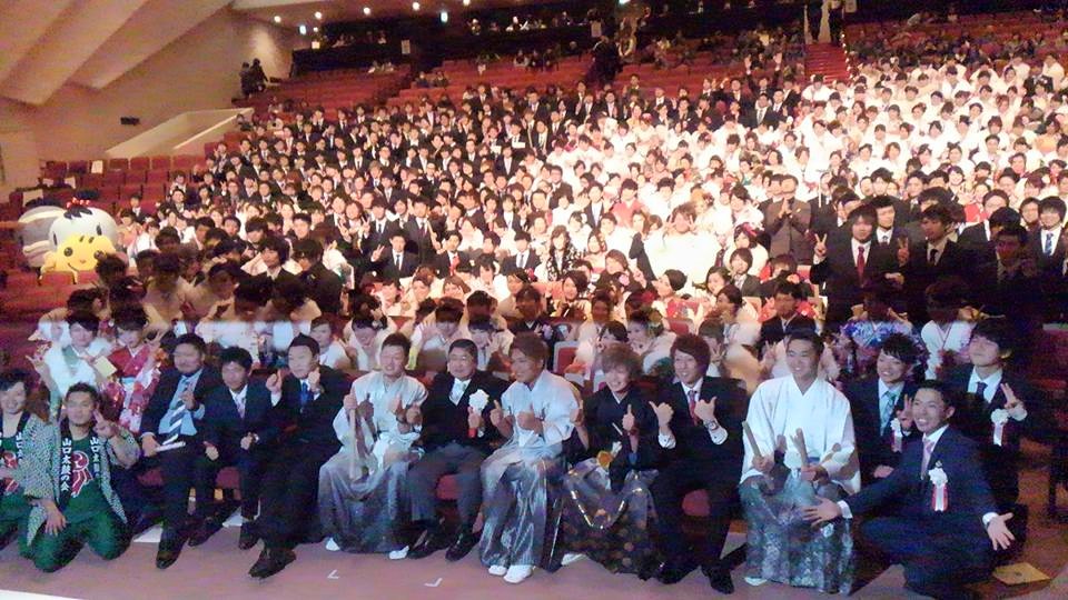 袴やスーツ、着物を着た新成人たちが会場の椅子に座っている記念写真