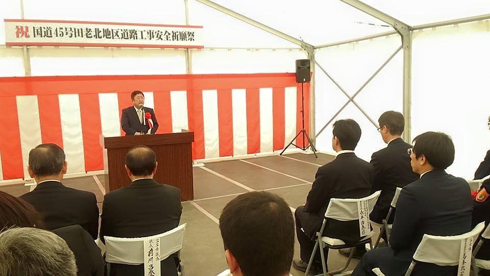 「祝 国道45号田老北地区道路工事安全祈願祭」と書かれた横断幕と紅白幕が掛かったテントの中で、演台のマイクに向かい話をする市長とパイプ椅子に座る関係者の方々の写真