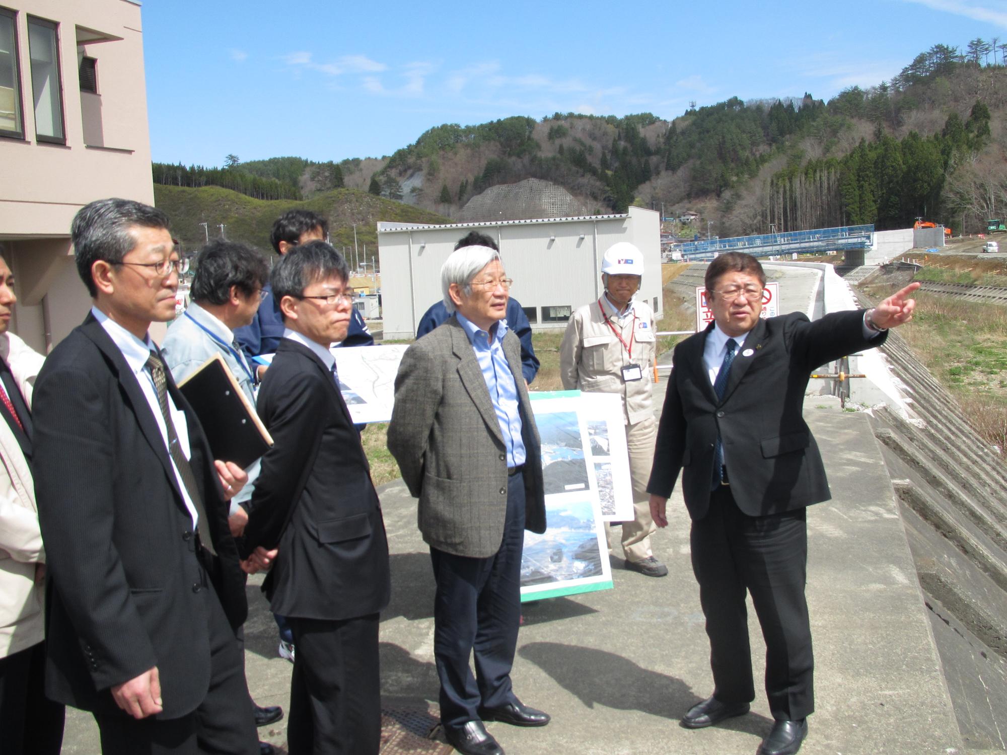 市長が元東日本大震災復興構想会議議長の五百旗頭真氏に指をさして、復興状況を説明しているのを同行して視察に来られた方々も聞いている写真