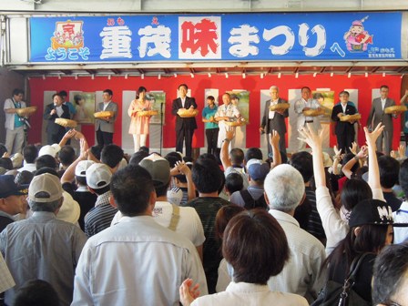 紅白幕が壁に張られ「ようこそ重茂味まつりへ」と掲げられた横断幕の下、市長と関係者がステージ上に上がっており、参加者側からステージを見ている写真