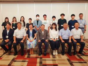前列で椅子に座る7名と後列で立って横一列に並ぶ10名の学生と関係者たちを写した記念写真