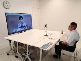 白色で統一された部屋で市長が席に座り、モニターに映っている女性とオンラインで意見交換している写真