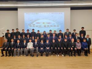 壁のスクリーン前に「宮古地区学生研究・意見発表会」に参加した高校生と関係者が3列に並んで記念撮影をしている写真