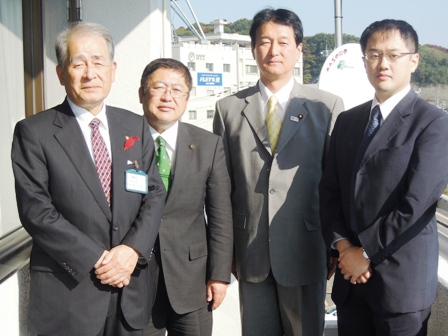 建物の外で市長と大島敦総務副大臣と関係者2名が横で並んでいる写真