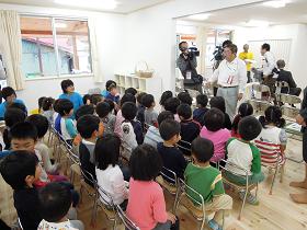田老保育所の仮設保育所の室内で、背筋を伸ばし椅子に座る園児達の前で話をする市長の写真