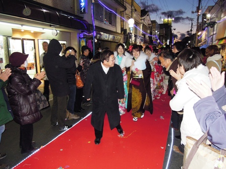 商店街の中央に引かれたレッドカーペットの上を市長を先頭に新成人たちが一緒に歩いている写真