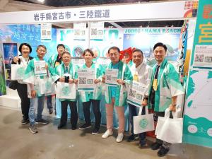 エメラルドグリーンと白が基調のお揃いの法被を着た宮古市の関係者が「日本東北遊楽日・だいすき東北」に参加し記念撮影をしている写真