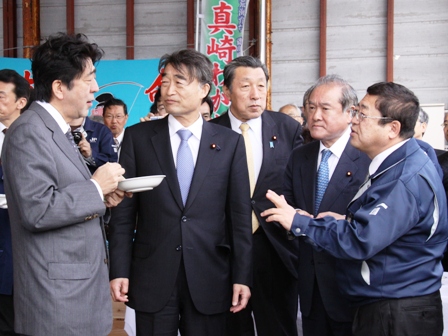 関係者に囲まれる中、魚市場内で安倍晋三首相と市長が向かい合い話をしている写真