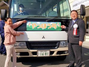 地域バスのフロントガラスの下に「やっほう号」と書かれたシールが貼られ、愛称を命名した川井小学校5年の藤田亜久理さんと市長がシールを指さしている様子の写真