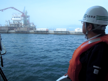 ヘルメットとライフジャケットを着用した市長が宮古港竜神崎防波堤の復旧工事を海上の船から見学している写真