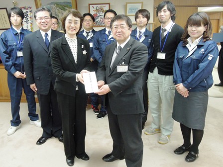 市長と山田恵美子副区長が両手で目録に手を添えており、その後ろで関係者達が横に並んでいる写真