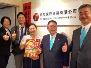 日盟国際商務有限公司の看板の前で赤い紙袋を持った女性と市長、女性の後ろに男性2名と市長の横に宮古市の関係者1名が並んで記念撮影をしている写真