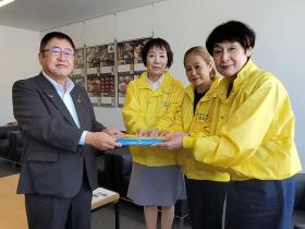 黄色のジャンパーを着た3人の女性から、市長がフェイスシールドを受け取る写真