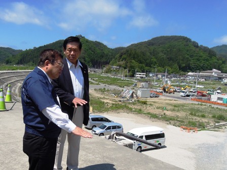 大空の下、宮古市の防波堤で説明をする市長と、話に耳を傾ける佐藤茂雄取締役相談役の写真