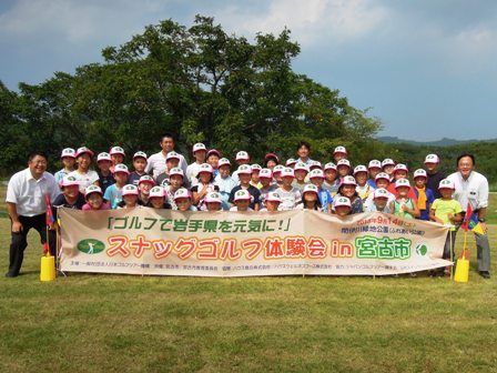 大空の下「スナッグゴルフ体験会 in 宮古市」と書かれた横断幕を手に持った子供達と市長と関係者が、横に3列で並んでいる写真