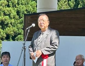 腰元に胸章を着けスタンドマイクの前で話をしている様子の市長の写真