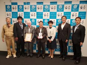 寄附金の目録を市長が持ち、市からの感謝状を持った眞木建設株式会社の方々と 他の市職員、計7人で並んで撮影した写真
