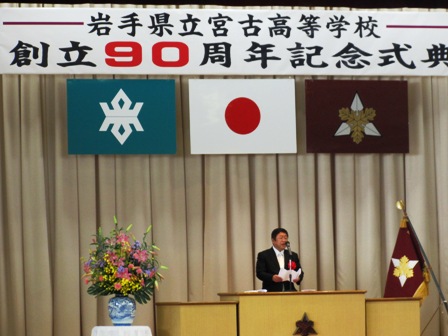 「岩手県立宮古高等学校 創立90周年記念式典」と書かれた横断幕、日本国旗や校旗が掲げられた舞台上で、演台のマイクに向かい話をする市長の写真