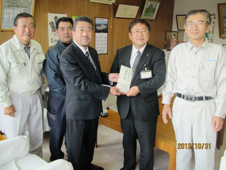 寄附金の封筒を一緒に持つ市長と男性のを中心に、男性3名が並ぶ記念写真
