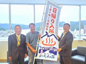 「日帰り入浴」と書かれた幟を持つ男性と市長、左端にもう1名の男性が並んで写っている写真