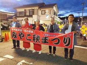 「みやこ秋祭り」と書かれた赤い横断幕を持つ5名の男性を写した写真