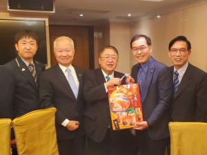 5人の中央に市長が赤い紙袋を右から2番目の男性と一緒にもちながら記念撮影をしている写真