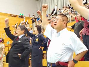 体育館の観覧席で市長と大勢の観客の方々が右手を上に掲げている様子の写真