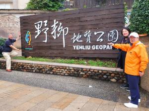 入り口にある野柳地質公園の案内板を指さししている市長と、右に女性、左に男性が並び記念撮影をしている写真