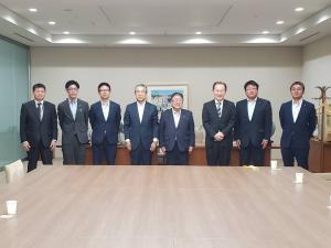 大きな茶色いテーブルが置かれた部屋の後方で、中央に立つ市長と7名の関係者の方々が横一列に並ぶ記念写真