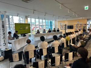 前方にパネリストや司会の方が座り、向かいにある観覧席に10数名の方が座って話を聞いている様子の写真
